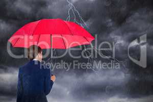 Composite image of rear view of businesswoman carrying red umbrella