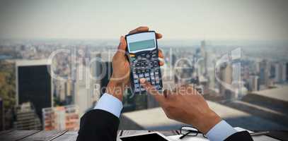 Composite image of cropped hands of businessman using calculator