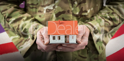 Composite image of mid section of soldier holding model home