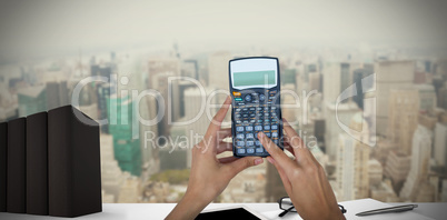 Composite image of cropped hands of businesswoman using calculator