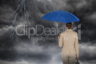 Composite image of rear view of businesswoman carrying blue umbrella