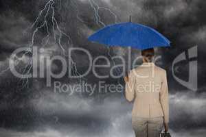 Composite image of rear view of businesswoman carrying blue umbrella