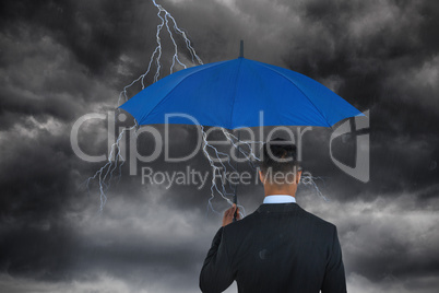 Composite image of rear view of businessman carrying blue umbrella