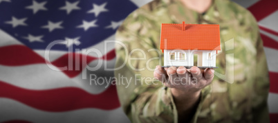 Composite image of mid section of soldier holding model house