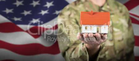 Composite image of mid section of soldier holding model house