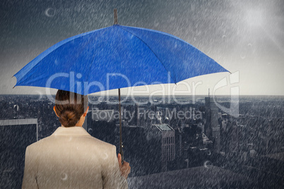 Composite image of rear view of businesswoman carrying blue umbrella