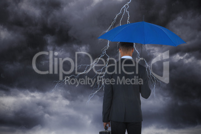 Composite image of rear view of businessman carrying blue umbrella and briefcase