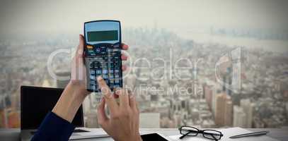 Composite image of hands of businesswoman using calculator