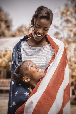 Happy mother and daughter wrapped in American flag at park