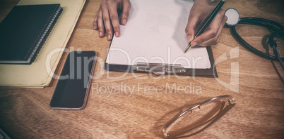 Cropped hands of doctor writing prescription on clipboard at desk