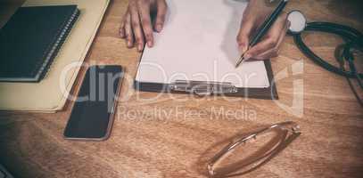 Cropped hands of doctor writing prescription on clipboard at desk