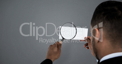 Composite image of rear view of man holding magnifying glass on paper