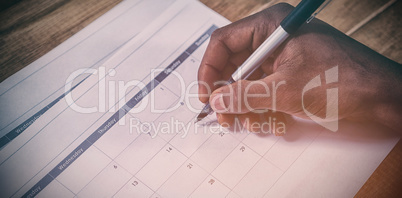 Cropped hand of businessman marking dates on calendar