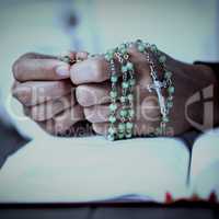 Praying hands of woman with rosary and bible