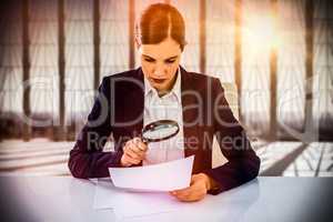 Composite image of businesswoman looking at document through magnifying glass