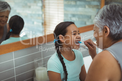 Grandmother helping granddaughter brush her teeth in the bathroom