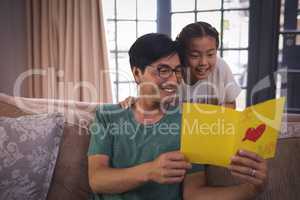 Father and daughter reading greeting card in living room