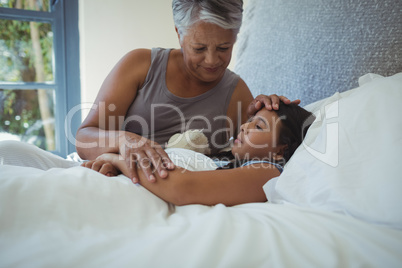 Grandmother comforting sick granddaughter in bed room