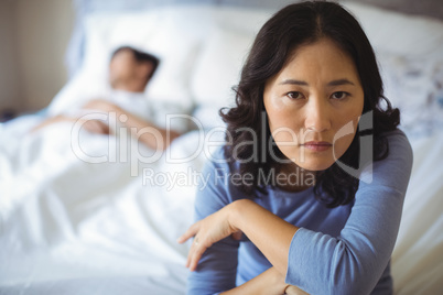 Upset woman sitting on bed in bedroom