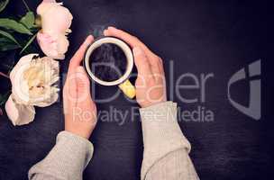 Cup of coffee in female hand on black background