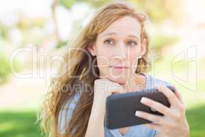 Concerned Young Woman Outdoors Looking At Her Smart Phone.