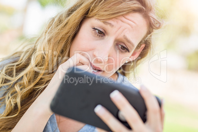 Concerned Young Woman Outdoors Looking At Her Smart Phone.