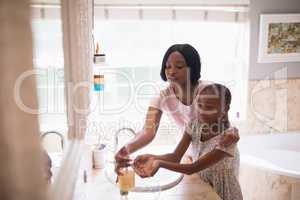 Mother assisting daughter while washing hands in bathroom