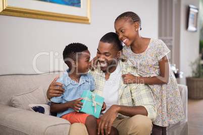 Father and children holding gift box on sofa at home