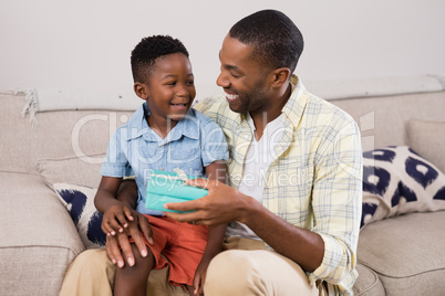 Cheerful father exchanging gift box on sofa