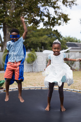 Playful siblings in costumes jumping on trampoline