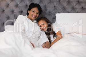 Smiling grandmother and granddaughter relaxing on bed at home