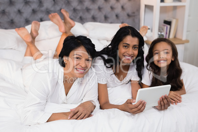 Portrait of smiling multi-generation family using digital tablet while lying on bed