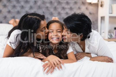 Grandmother and mother kissing smiling girl while lying on bed