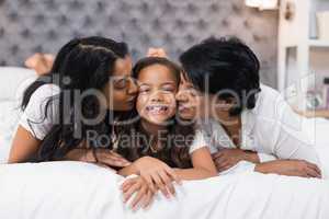 Grandmother and mother kissing smiling girl while lying on bed