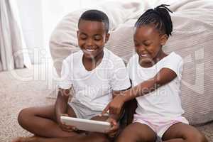 Cheerful siblings using digital tablet while sitting on rug