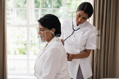 Nurse examining mature woman resting on bed at home