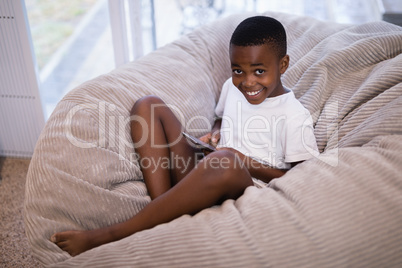 Portrait of smiling boy using mobile phone while sitting on couch at home