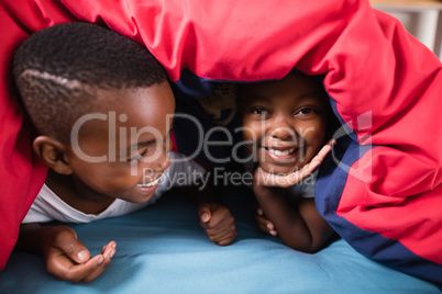 Happy siblings playing under blanket at home