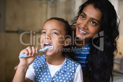 Smiling mother standing by daughter brushing teeth in bathroom