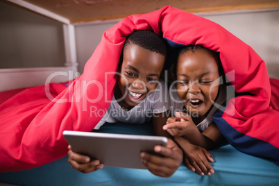 Cheerful siblings using digital tablet while lying on bed