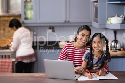 Portrait of smiling girl with mother studying in kitchen