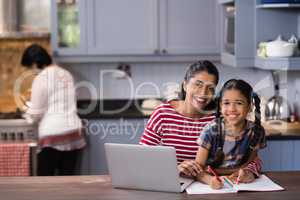 Portrait of smiling girl with mother studying in kitchen