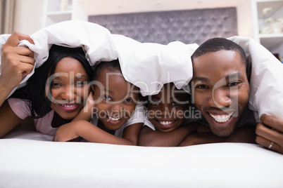 Portrait of happy family lying together under blanket on bed