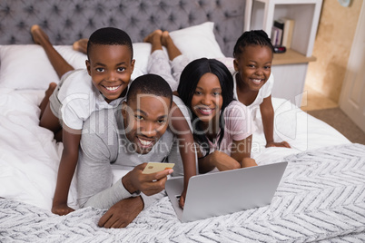 Portrait of happy family shopping online on bed