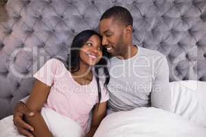 Smiling couple embracing while sitting on bed