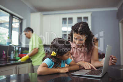 Mother and daughter using laptop in kitchen