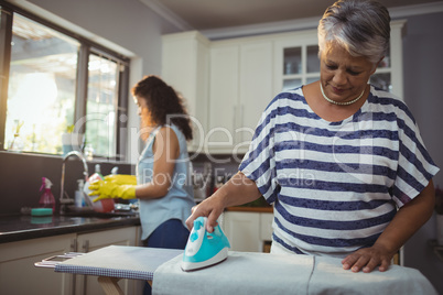 Mother ironing clothes while daughter washing utensil