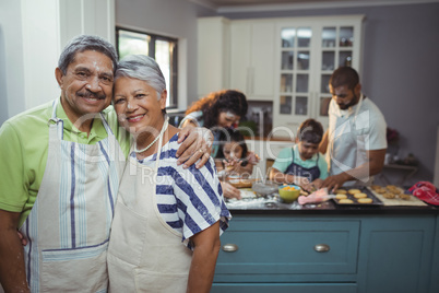 Senior couple smiling at camera while family members preparing dessert in background