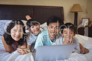 Happy family doing online shopping on laptop in the bed room