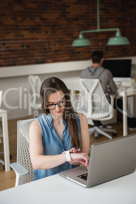 Female executive adjusting smart watch at desk